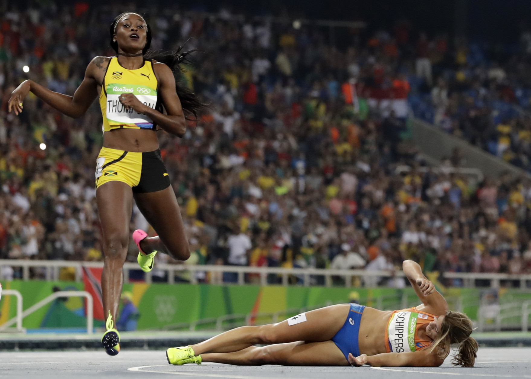 Second placed Netherlands' Dafne Schippers lies on the ground after falling over the finish line as Elaine Thompson from Jamaica, left, wins the gold in the women's 200-meter final during the athletics competitions of the 2016 Summer Olympics at the Olympic stadium in Rio de Janeiro, Brazil, Wednesday, Aug. 17, 2016. (AP Photo/David J. Phillip)