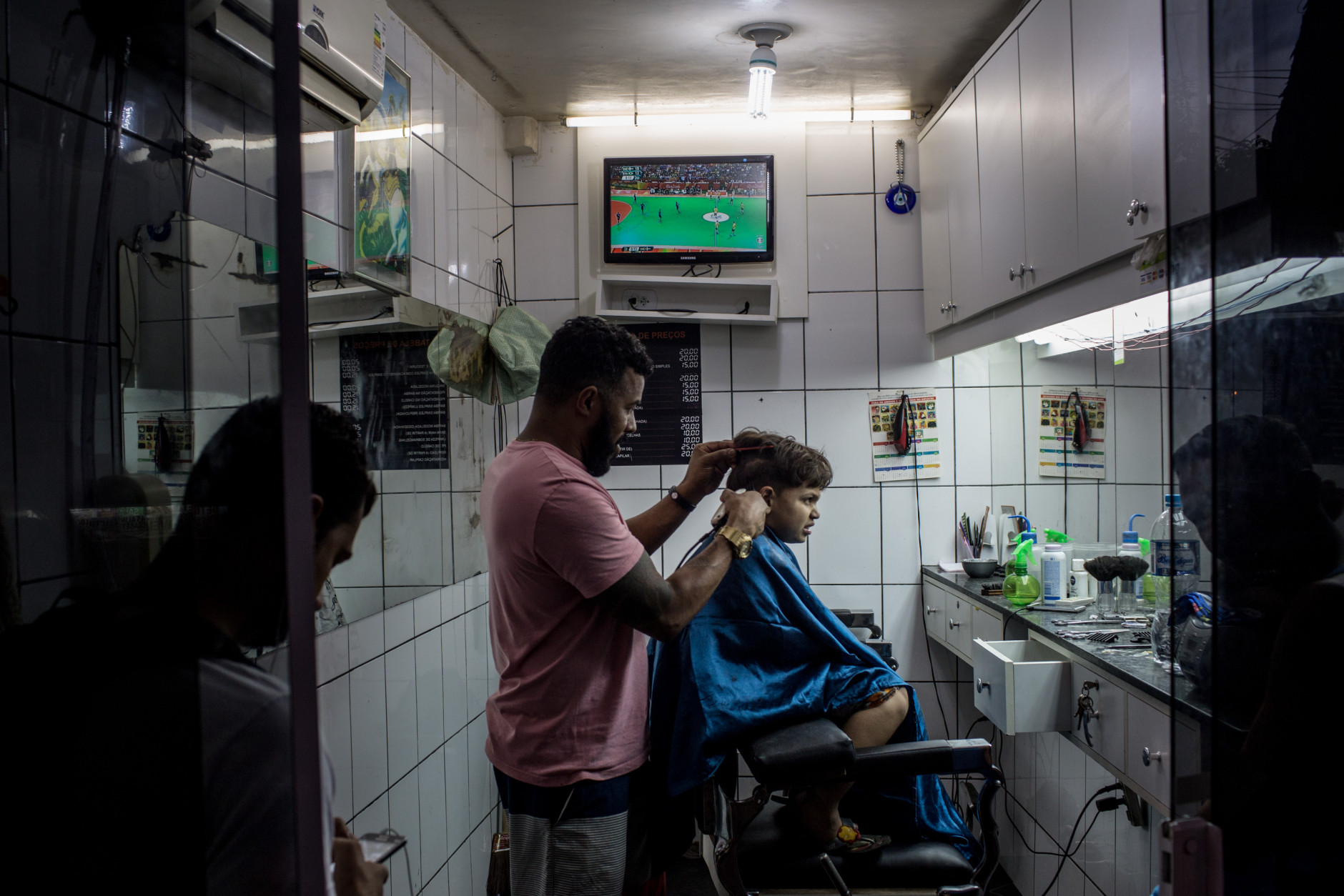 RIO DE JANEIRO, BRAZIL - AUGUST 15:  A young boy grimaces while getting his haircut as the Olympic games is shown on a tv screen at a hair salon on the outskirts of a 'favela' community on August 15, 2016 in Rio de Janeiro, Brazil.  Brazil is currently hosting the 2016 Summer Olympic games despite the dismissal of President Dilma Rousseff, pollution concerns, ongoing crime problems and a failing economy. Around 1.4 million residents, or approximately 22 percent of Rio's population, reside in favelas which often lack proper sanitation, health care, education and security, for many of these residents watching the Olympic games on tv is their only access to the event.  (Photo by Chris McGrath/Getty Images)