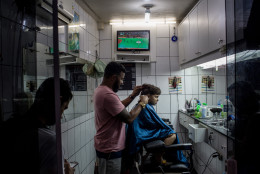 RIO DE JANEIRO, BRAZIL - AUGUST 15:  A young boy grimaces while getting his haircut as the Olympic games is shown on a tv screen at a hair salon on the outskirts of a 'favela' community on August 15, 2016 in Rio de Janeiro, Brazil.  Brazil is currently hosting the 2016 Summer Olympic games despite the dismissal of President Dilma Rousseff, pollution concerns, ongoing crime problems and a failing economy. Around 1.4 million residents, or approximately 22 percent of Rio's population, reside in favelas which often lack proper sanitation, health care, education and security, for many of these residents watching the Olympic games on tv is their only access to the event.  (Photo by Chris McGrath/Getty Images)