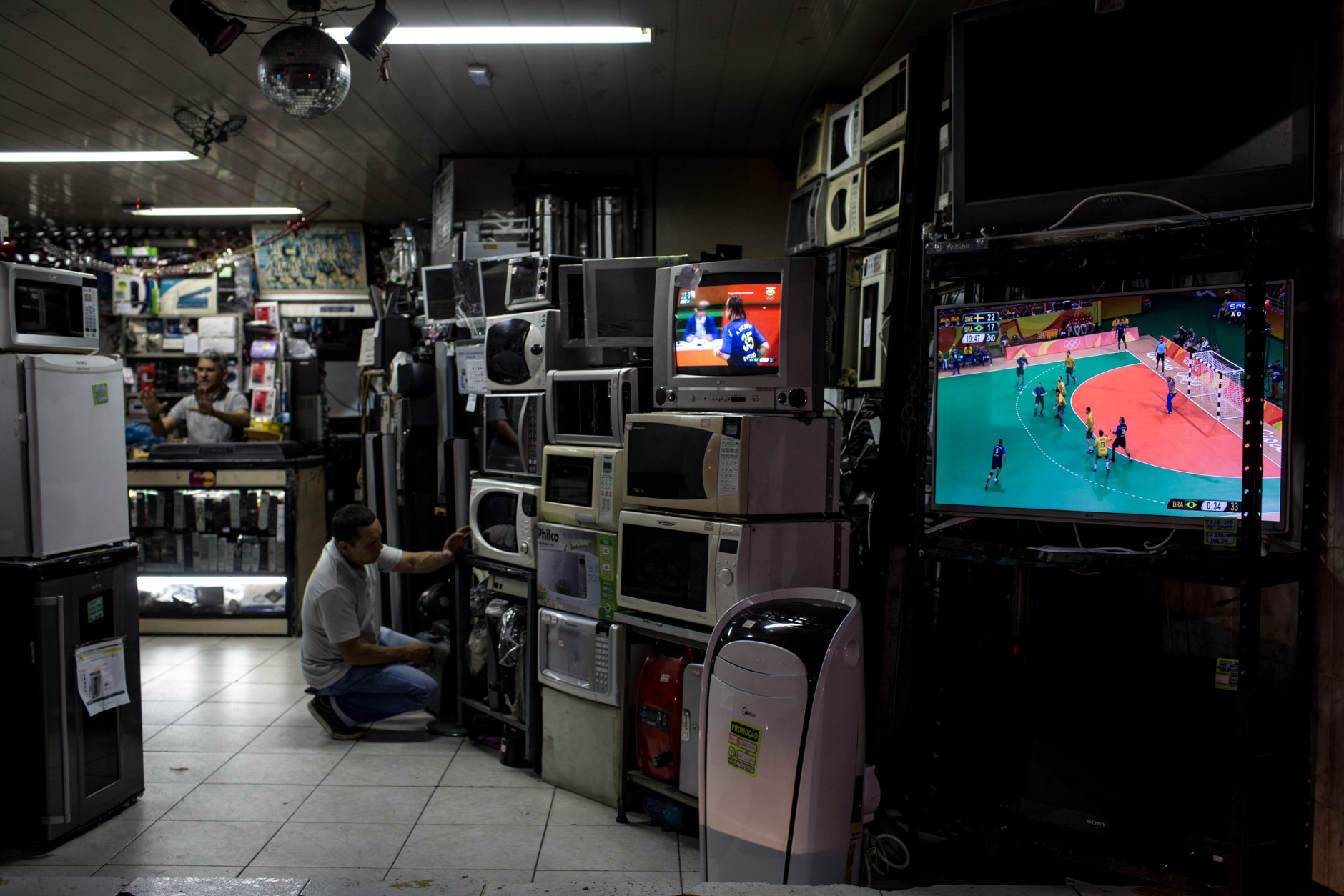 RIO DE JANEIRO, BRAZIL - AUGUST 15:  A man works at an electronics store as the Olympic games is shown on tv screens on August 15, 2016 in Rio de Janeiro, Brazil.  Brazil is currently hosting the 2016 Summer Olympic games despite the dismissal of President Dilma Rousseff, pollution concerns, ongoing crime problems and a failing economy. Around 1.4 million residents, or approximately 22 percent of Rio's population, reside in favelas which often lack proper sanitation, health care, education and security, for many of these residents watching the Olympic games on tv is their only access to the event.  (Photo by Chris McGrath/Getty Images)