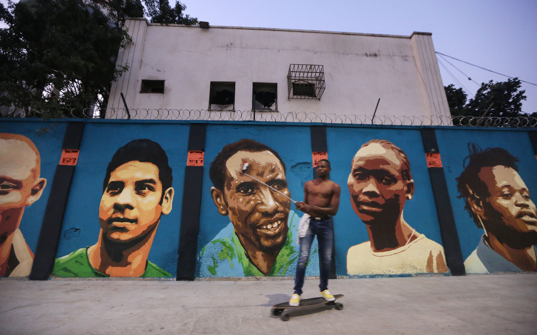 RIO DE JANEIRO, BRAZIL - AUGUST 17: A man skateboards while filming past a new mural of street art honoring the first Olympic refugee team during the Rio 2016 Olympic Games on August 17, 2016 in Rio de Janeiro, Brazil. The graffitti, created by the artists Rodrigo Sini and Cety Soledade, honors the stateless refugees, six men and four women, who hail from South Sudan, Syria, the Deomocratic Republic of Congo and Ethiopia. (Photo by Mario Tama/Getty Images)