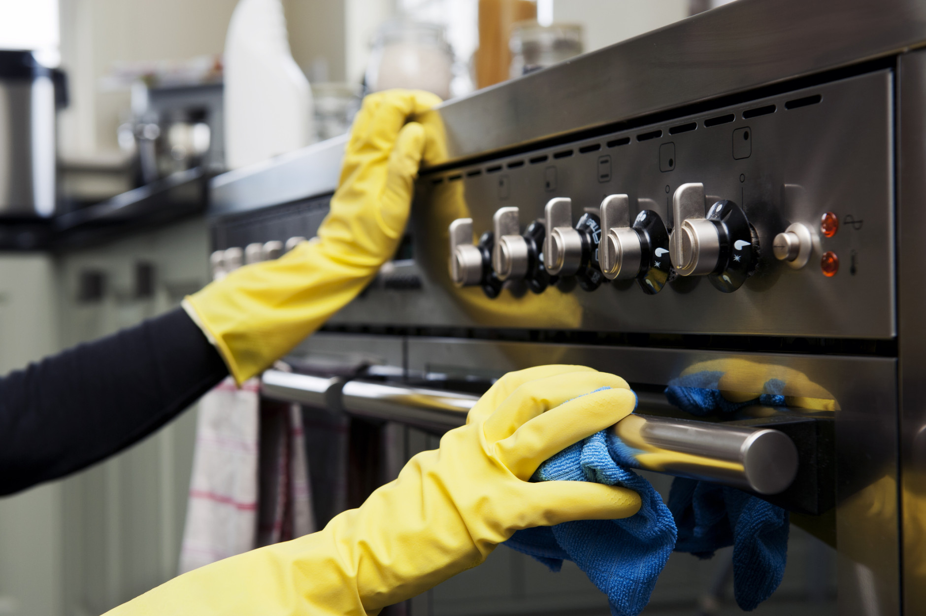 Closeup photograph of two hands cleaning the oven in a domestic kitchen.