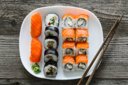 various sushi on white plate with chopsticks on wooden background