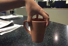 WTOP's Teta Alim demonstrates the typical way to carry a cup of coffee, and the "claw-hand" method, which a study says is better at preventing spilling. (WTOP/Michelle Basch)