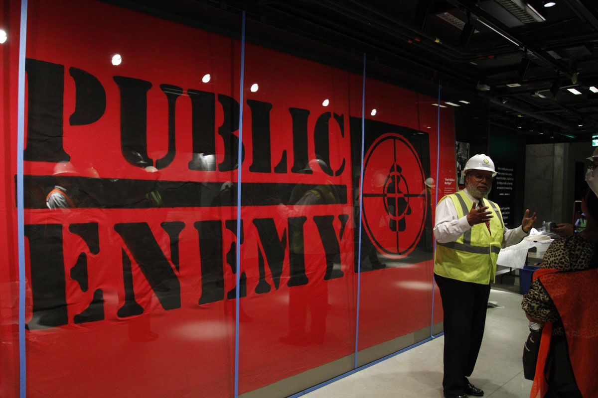 In this photo taken July 18, 2016, Museum Director Lonnie Bunch stands in-front of an art piece representing hip-hop group Public Enemy in the Smithsonian National Museum of African American History and Culture in Washington, during a media tour. The museum's grand opening will be on Sept. 24. (AP Photo/Paul Holston)
