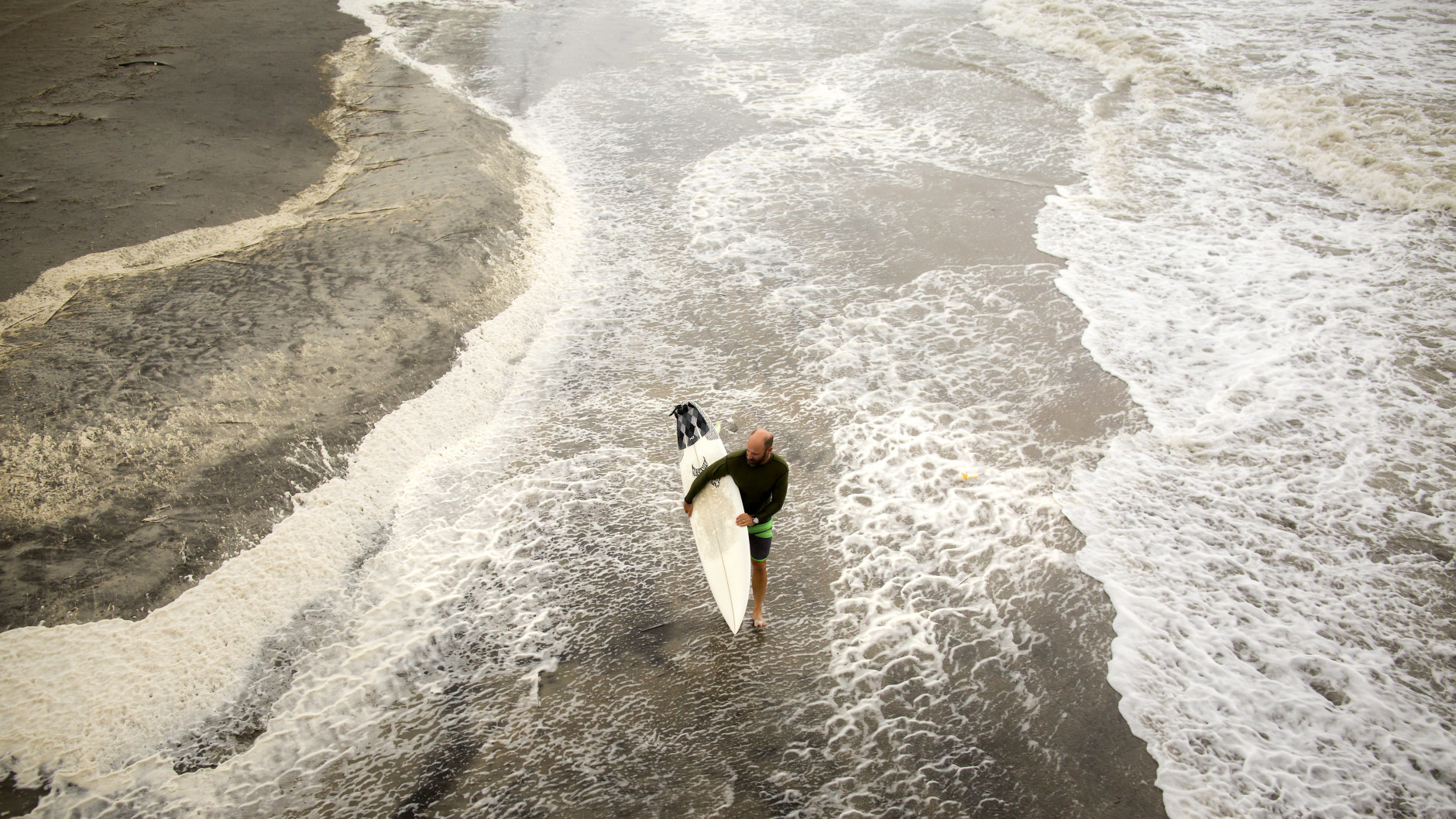 A surfer walks the beach while looking for waves from the surge of Hurricane Hermine, Friday, Sept. 2, 2016, off the coast of Tybee Island, Ga.  Hermine was downgraded to a tropical storm after it made landfall, as it moves over Georgia, but the U.S. National Hurricane Center says winds are increasing along the Southeast coast and flooding rains continue.  (AP Photo/Stephen B. Morton)
