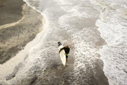 A surfer walks the beach while looking for waves from the surge of Hurricane Hermine, Friday, Sept. 2, 2016, off the coast of Tybee Island, Ga.  Hermine was downgraded to a tropical storm after it made landfall, as it moves over Georgia, but the U.S. National Hurricane Center says winds are increasing along the Southeast coast and flooding rains continue.  (AP Photo/Stephen B. Morton)