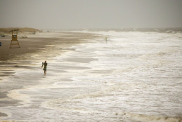 A surfer walks the beach while looking for waves from the surge of Hurricane Hermine, Friday, Sept. 2, 2016, off the coast of Tybee Island, Ga.  Hermine was downgraded to a tropical storm after it made landfall, as it moves over Georgia, but the U.S. National Hurricane Center says winds are increasing along the Southeast coast and flooding rains continue.  (AP Photo/Stephen B. Morton)