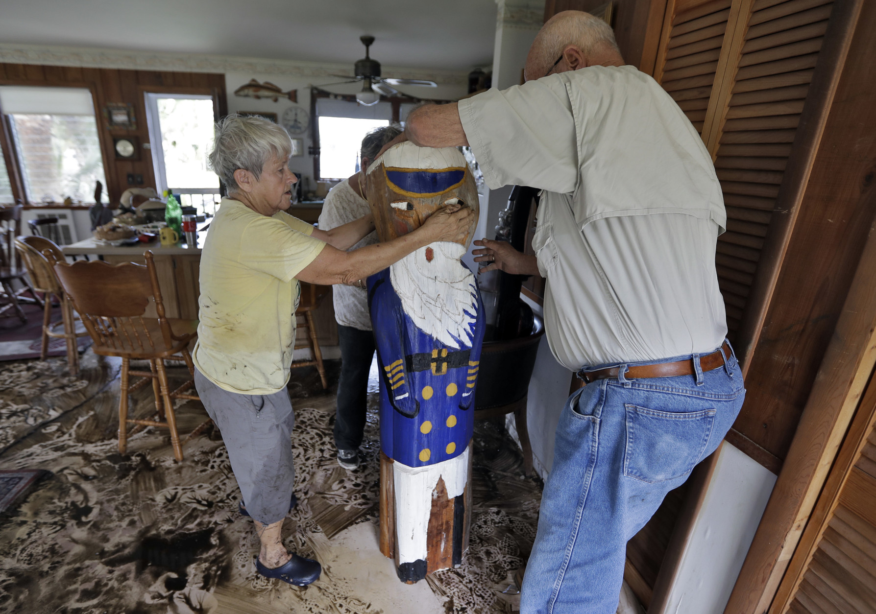 Bobbi Pattison, left, with help from her neighbors Hugh and Harriet Oglesby, stands up a sea captain statue carved out of wood from a 1993 storm at her home Friday, Sept. 2, 2016, in Steinhatchee, Fla. Hurricane Hermine was downgraded to a tropical storm after it made landfall, as it moves over Georgia, but the U.S. National Hurricane Center says winds are increasing along the Southeast coast and flooding rains continue. (AP Photo/Chris O'Meara)