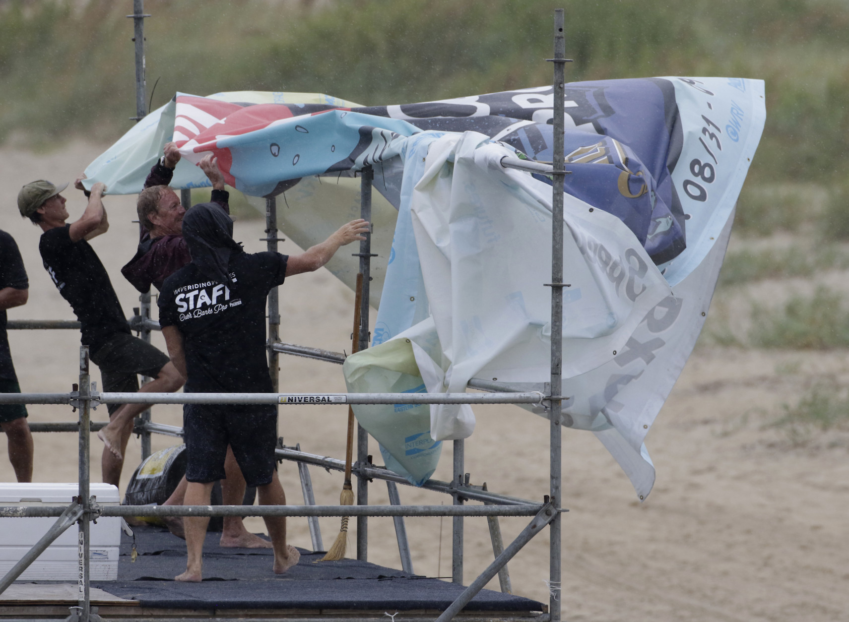 Staff members for the MRV Outer Banks Pro surf tournament take down a banner in Nags Head, N.C., Friday, Sept. 2, 2016, as Tropical Storm Hermine heads toward the Outer Banks. (AP Photo/Tom Copeland)