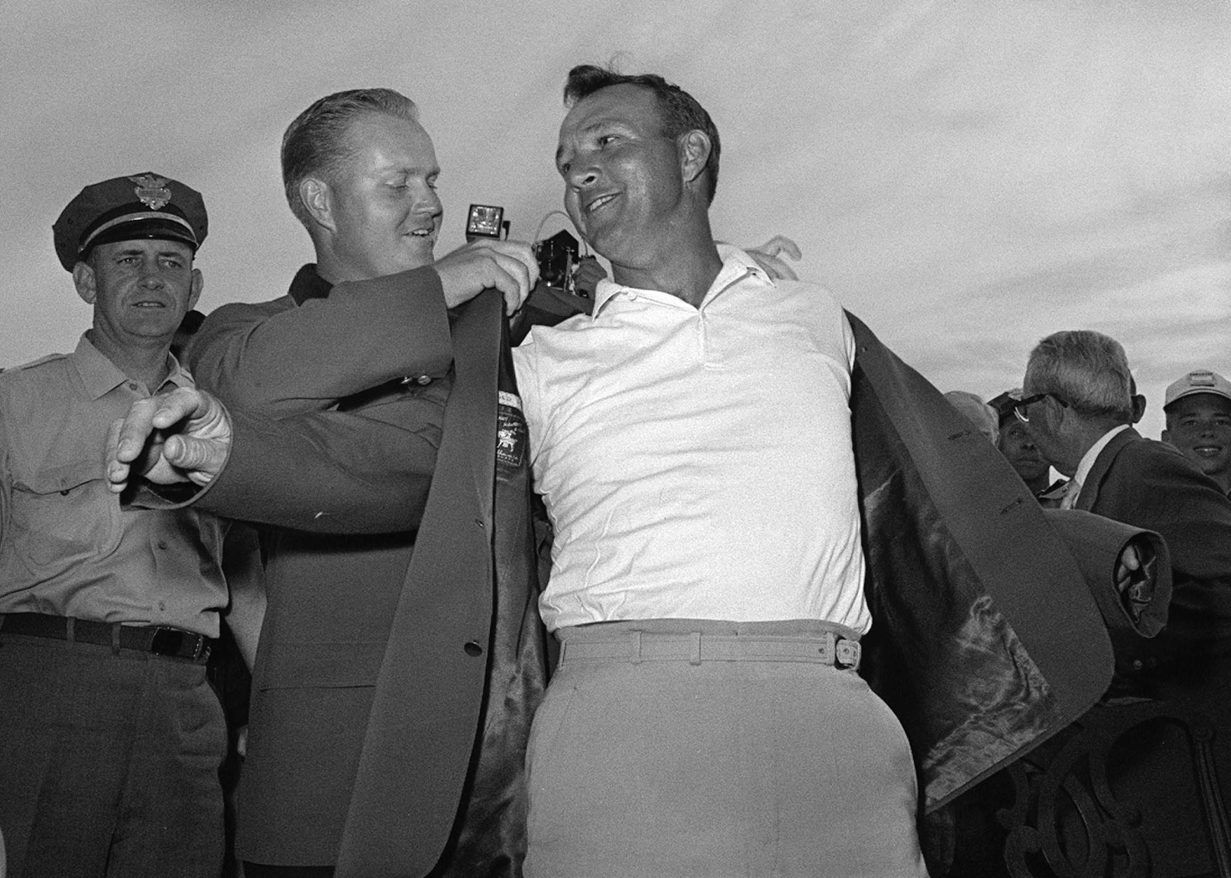 FILE - In this April 12, 1964 file photo, Arnold Palmer, right, slips into his green jacket with help from Jack Nicklaus after winning the Masters golf championship, in Augusta, Ga. Palmer, who made golf popular for the masses with his hard-charging style, incomparable charisma and a personal touch that made him known throughout the golf world as "The King," died Sunday, Sept. 25, 2016, in Pittsburgh. He was 87.  (AP Photo/File)