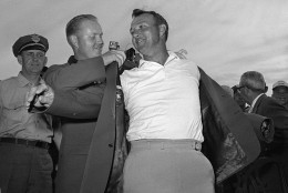 FILE - In this April 12, 1964 file photo, Arnold Palmer, right, slips into his green jacket with help from Jack Nicklaus after winning the Masters golf championship, in Augusta, Ga. Palmer, who made golf popular for the masses with his hard-charging style, incomparable charisma and a personal touch that made him known throughout the golf world as "The King," died Sunday, Sept. 25, 2016, in Pittsburgh. He was 87.  (AP Photo/File)
