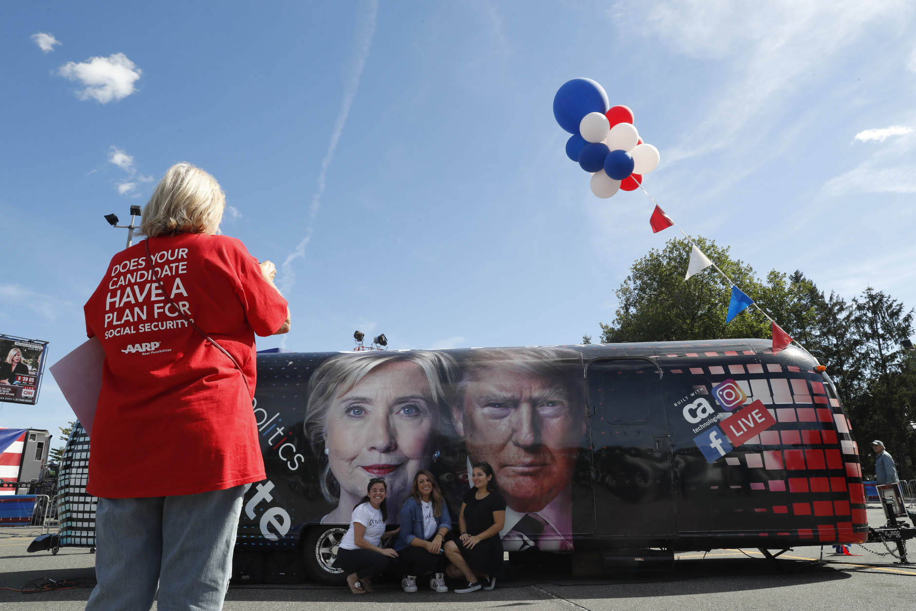 People pose for a photo kneeling near a bus adorned with photos of candidates Hillary Clinton and Donald Trump before the presidential debate at Hofstra University in Hempstead, N.Y., Monday, Sept. 26, 2016. (AP Photo/Mary Altaffer)