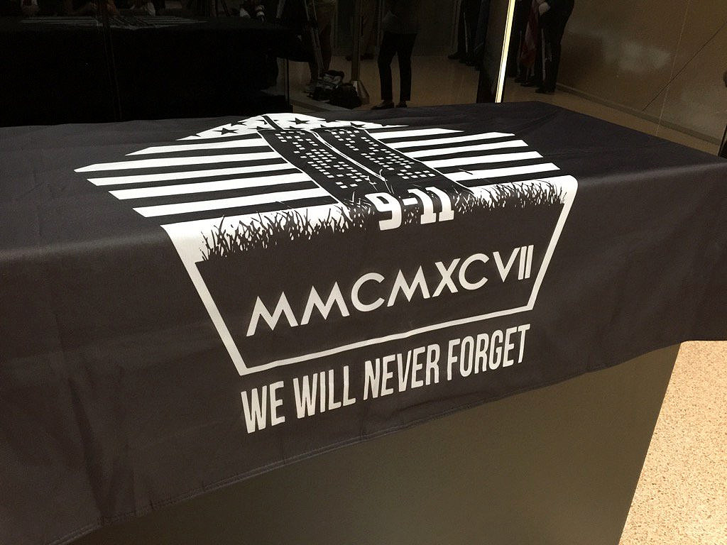 A black shroud with an image depicting the terror attacks at the Pentagon, the World Trade Center and the field in Shanksville, Pennsylvania, includes the Roman numeral 2,997 representing the number of victims killed on Sept. 11. A damaged piece limestone from the attack at the Pentagon was unveiled at Dulles International Airport on Thursday, Sept. 1, 2016. (WTOP/Kristi King)