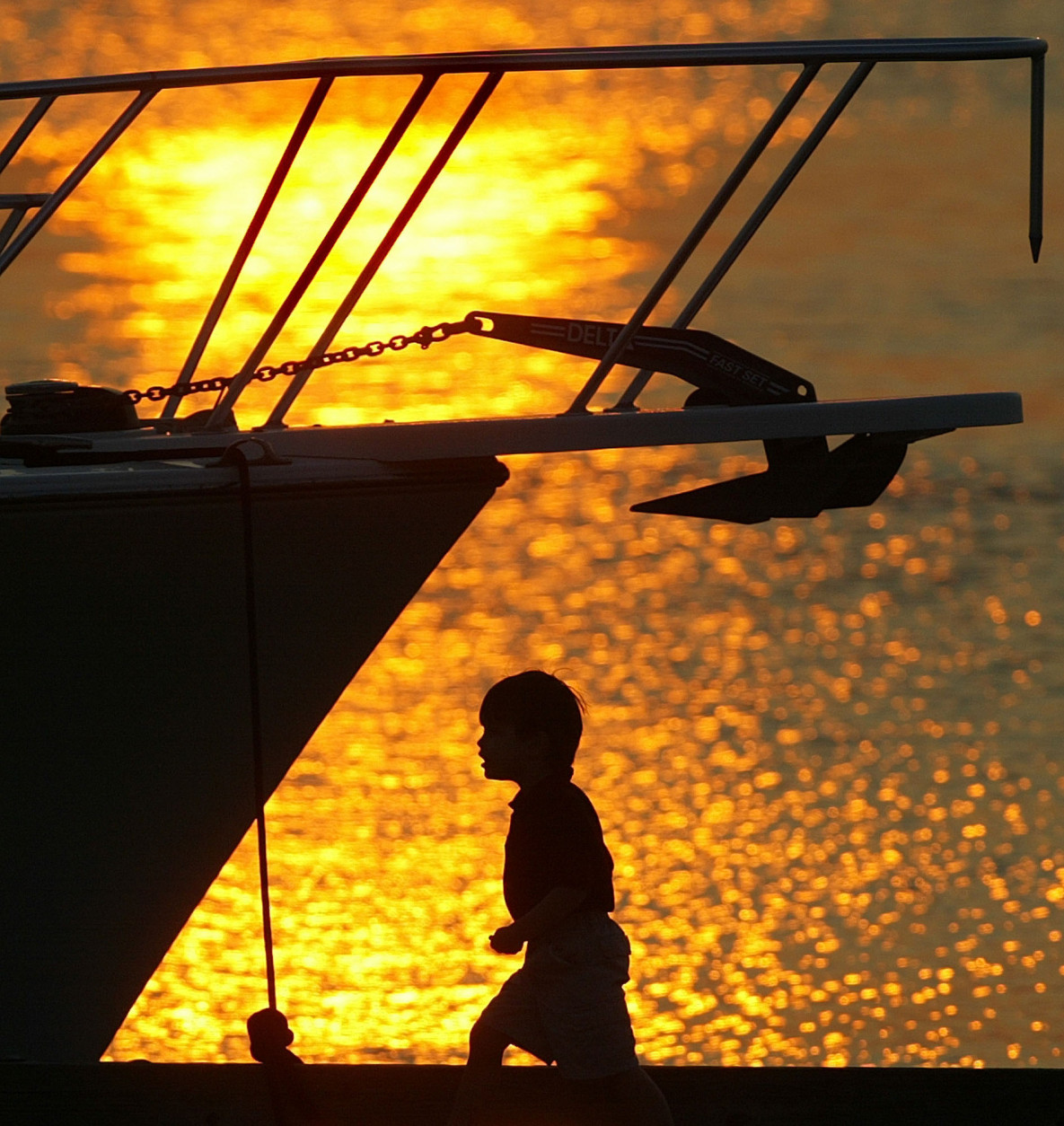 A child is silhouetted by the afternoon sun as he walks past a moored boat at an Intercoastal Waterway marina dock, Saturday, April 10, 2004, in Fernandina Beach, Fla. This area of north-east Florida is a well-know spot for viewing and photographing sunsets.(AP Photo/Phil Coale)