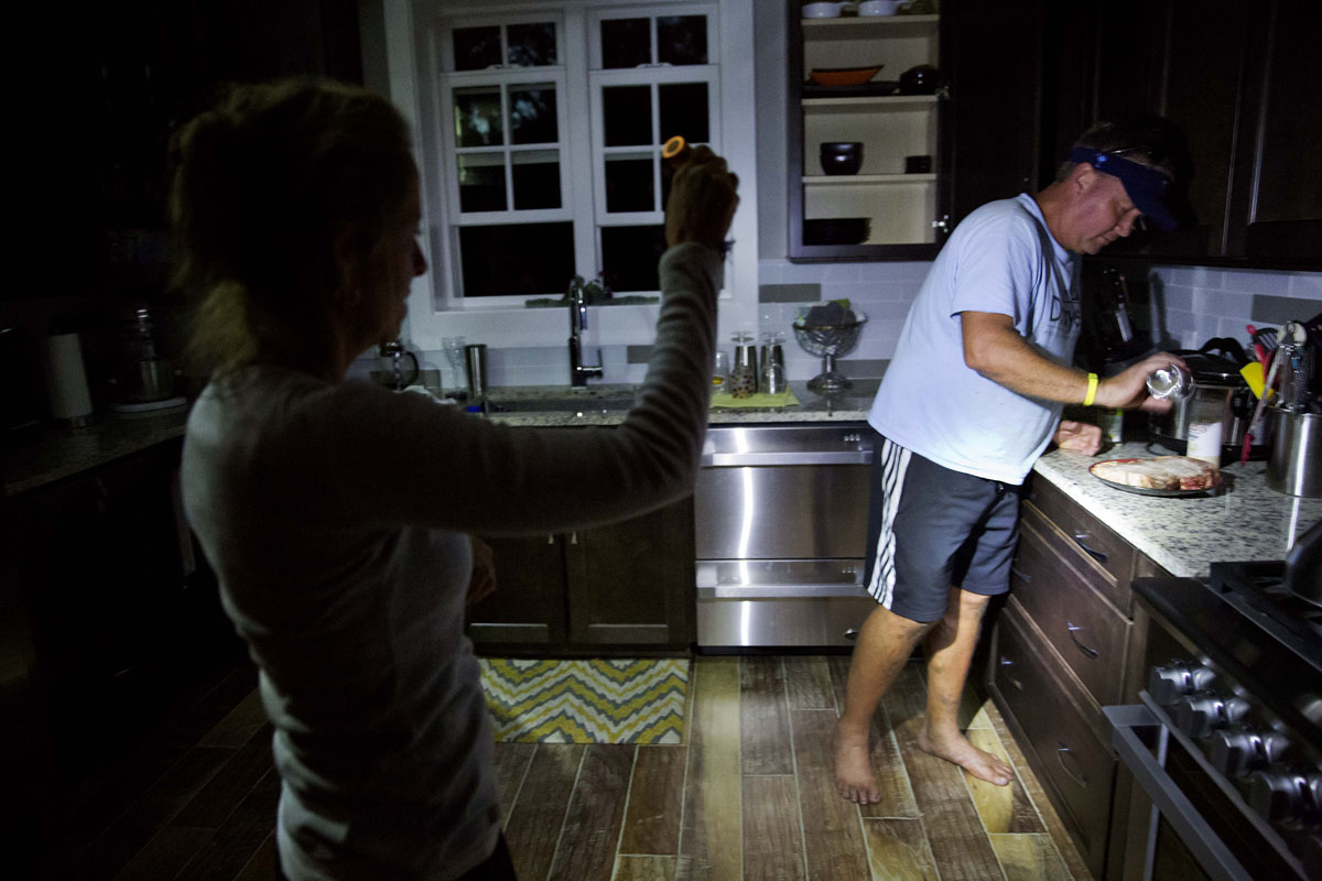 Missy Zinc, left, holds a flashlight for her husband Shawn as he prepares steaks for them to grill as they spend another night without power from Hurricane Matthew in Hilton Head, S.C., Sunday, Oct. 9, 2016. (AP Photo/David Goldman)