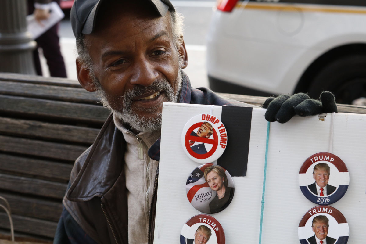 Steven Plummer was selling campaign buttons outside the Trump Hotel Oct. 26. He had his bases covered: with both Donald Trump and Hillary Clinton buttons available. With a smile, he said "For this particular crowd, we sold ...more Dump Trump buttons!" (WTOP/Kate Ryan)