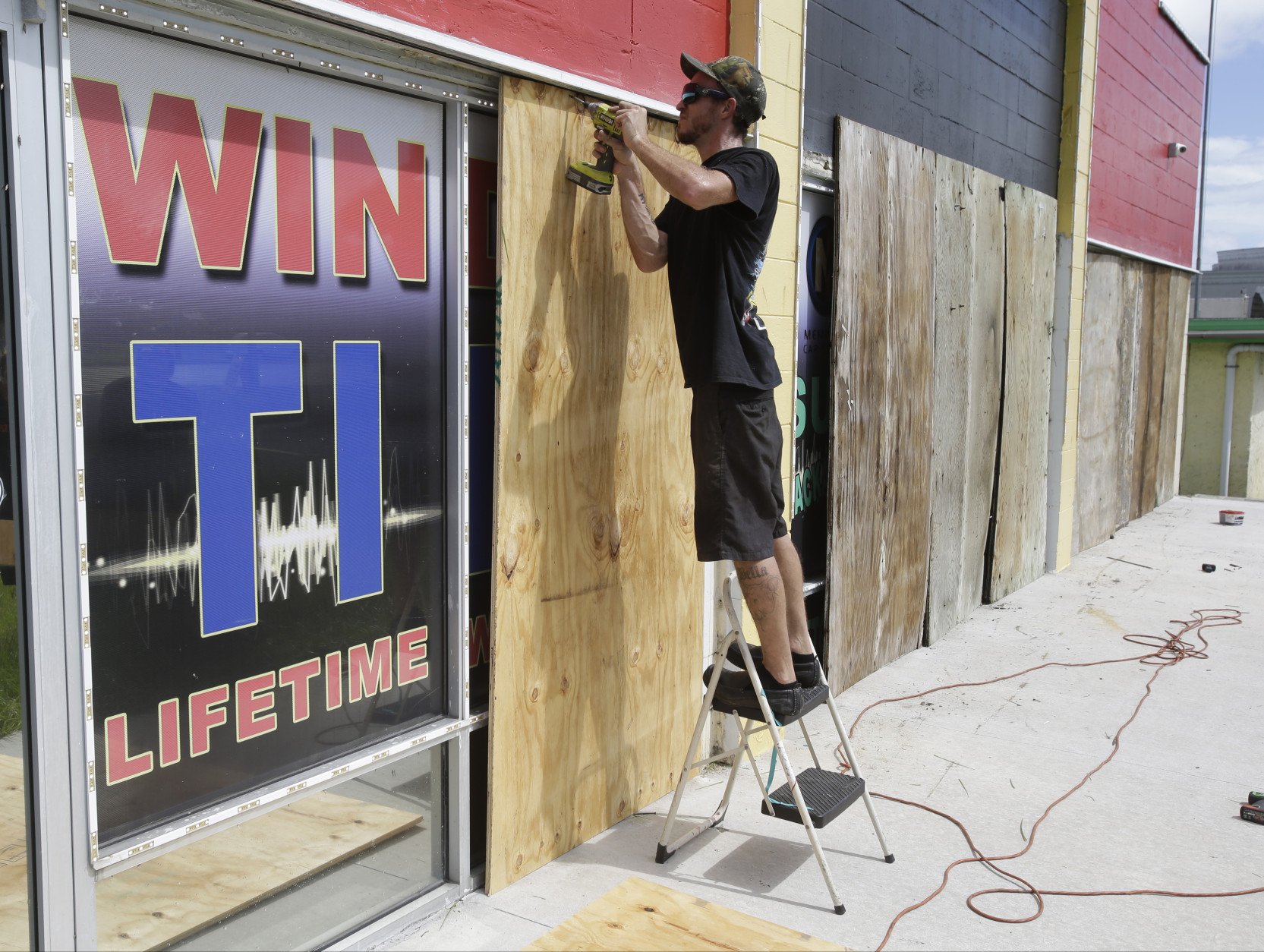 Chris Ramsey installs plywood panels over windows at a auto stereo and window tint shop in preparation for Hurricane Matthew, Wednesday, Oct. 5, 2016, in Cocoa Beach, Fla. (AP Photo/John Raoux)