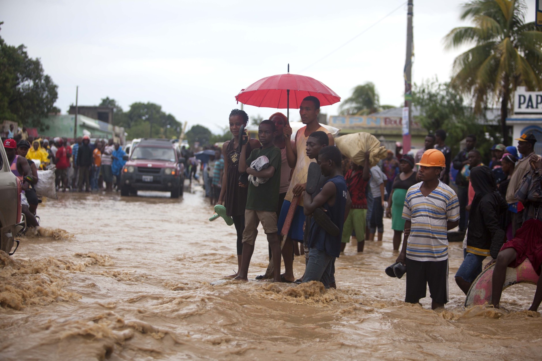 People stand in a street flooded by a nearby river overflowing from the heavy rains caused by Hurricane Matthew, in Leogane, Haiti, Wednesday, Oct. 5, 2016. Rescue workers in Haiti struggled to reach cutoff towns and learn the full extent of the death and destruction caused by Hurricane Matthew as the storm began battering the Bahamas on Wednesday and triggered large-scale evacuations along the U.S. East Coast. ( AP Photo/Dieu Nalio Chery)