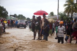 People stand in a street flooded by a nearby river overflowing from the heavy rains caused by Hurricane Matthew, in Leogane, Haiti, Wednesday, Oct. 5, 2016. Rescue workers in Haiti struggled to reach cutoff towns and learn the full extent of the death and destruction caused by Hurricane Matthew as the storm began battering the Bahamas on Wednesday and triggered large-scale evacuations along the U.S. East Coast. ( AP Photo/Dieu Nalio Chery)