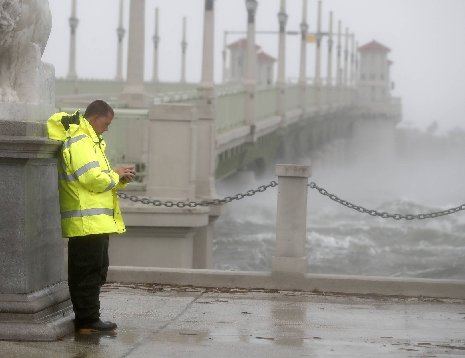 A police officer tries to shield himself from winds from Hurricane Matthew behind statue as he checks his cell phone Friday, Oct. 7, 2016, in St. Augustine , Fla.  Matthew was downgraded to a Category 3 hurricane overnight, and its storm center hung just offshore as it moved up the Florida coastline, sparing communities its full 120 mph winds.   (AP Photo/John Bazemore)