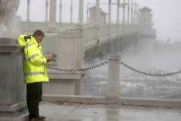 A police officer tries to shield himself from winds from Hurricane Matthew behind statue as he checks his cell phone Friday, Oct. 7, 2016, in St. Augustine , Fla.  Matthew was downgraded to a Category 3 hurricane overnight, and its storm center hung just offshore as it moved up the Florida coastline, sparing communities its full 120 mph winds.   (AP Photo/John Bazemore)
