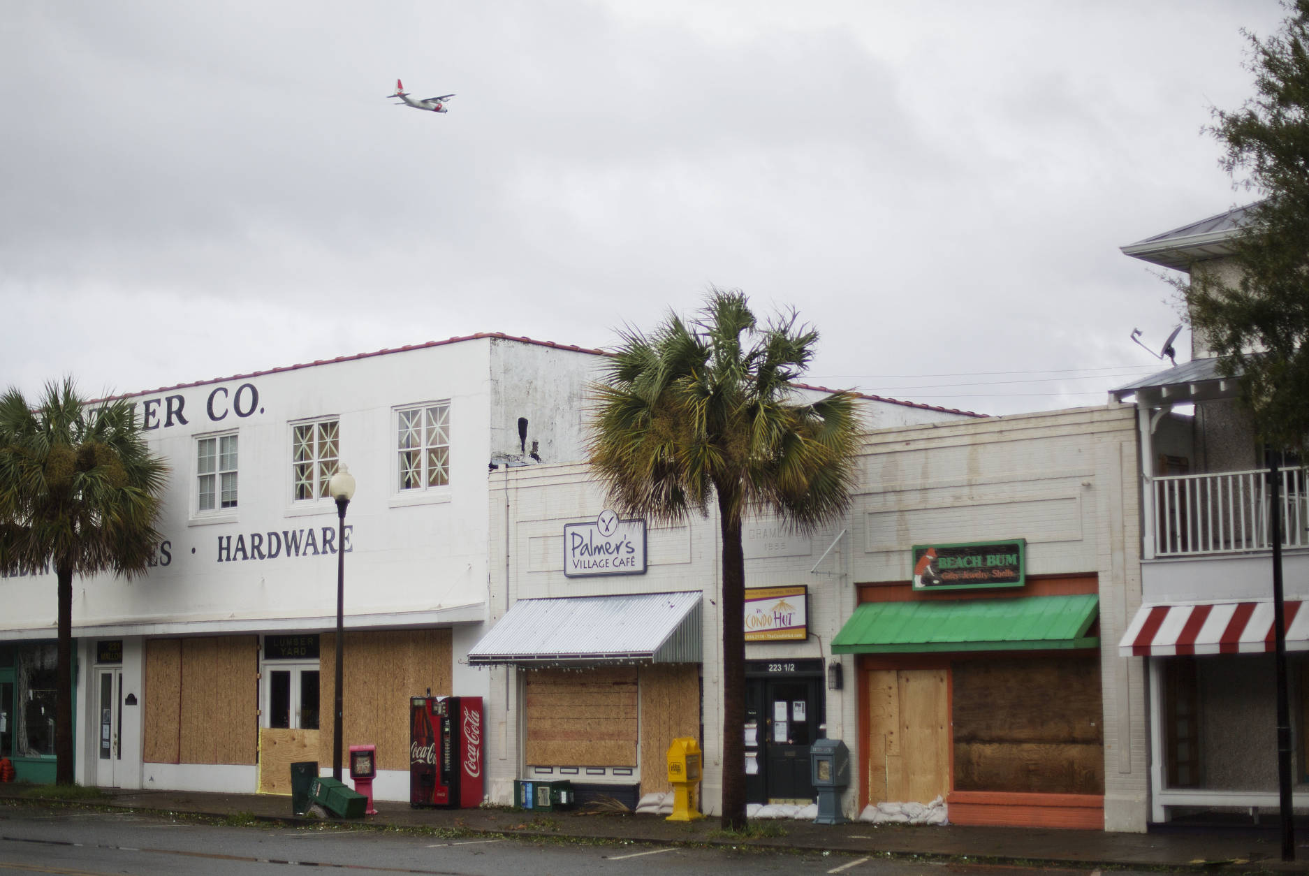 A U.S. Coast Guard plane flies over boarded up shops after Hurricane Matthew passed through St. Simons Island, Ga., Saturday, Oct. 8, 2016. A weakening Hurricane Matthew continued its march along the Atlantic coast Saturday, lashing two of the South's most historic cities and some of its most popular resort islands, flattening trees, swamping streets and knocking out power to hundreds of thousands. (AP Photo/David Goldman)