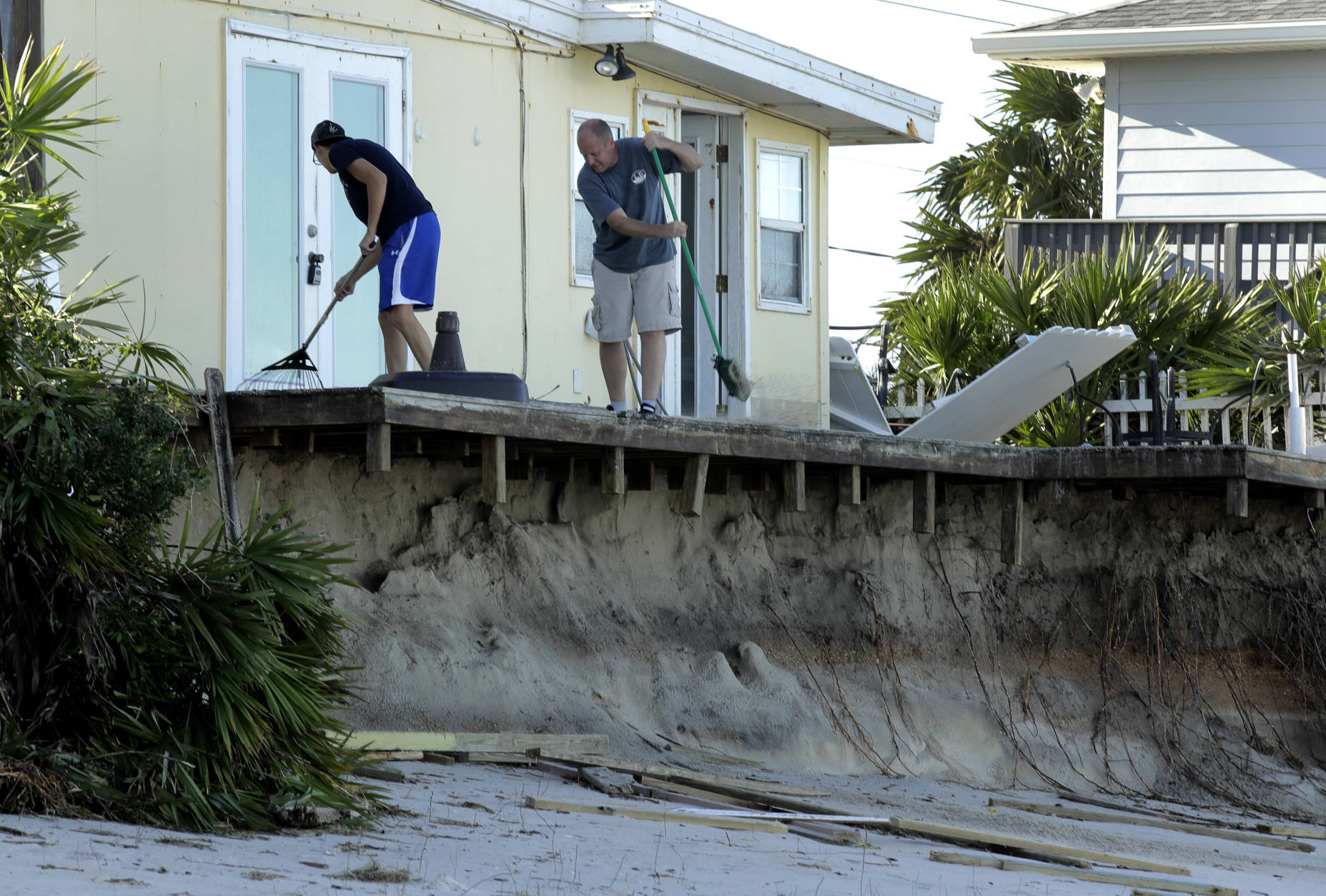 Rob Jakoby and his son Jake sweep debris off the eroded deck at his damaged beach home at Ponte Vedra Beach, Fla., Saturday, Oct. 8, 2016, after Hurricane Matthew passed through Friday. (AP Photo/Charlie Riedel)