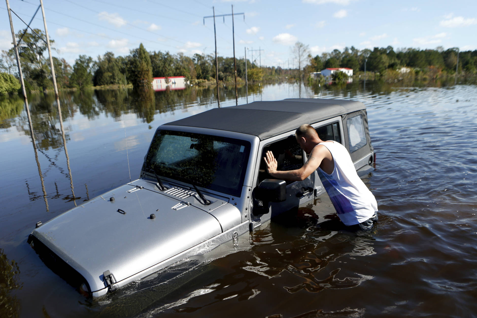After coming across a Jeep surrounded by floodwaters associated with Hurricane Matthew,  Elmer McDonald inspects the interior to make certain nobody was inside as he makes his way through a strong current after checking on his own mobile home for the first time on Thursday, Oct. 13, 2016, in Lumberton, N.C.  About 1,200 Lumberton residents had to be evacuated by boat and plucked from their roofs by helicopters as the river crested; McDonald was one of thousands who evacuated. (AP Photo/Brian Blanco)