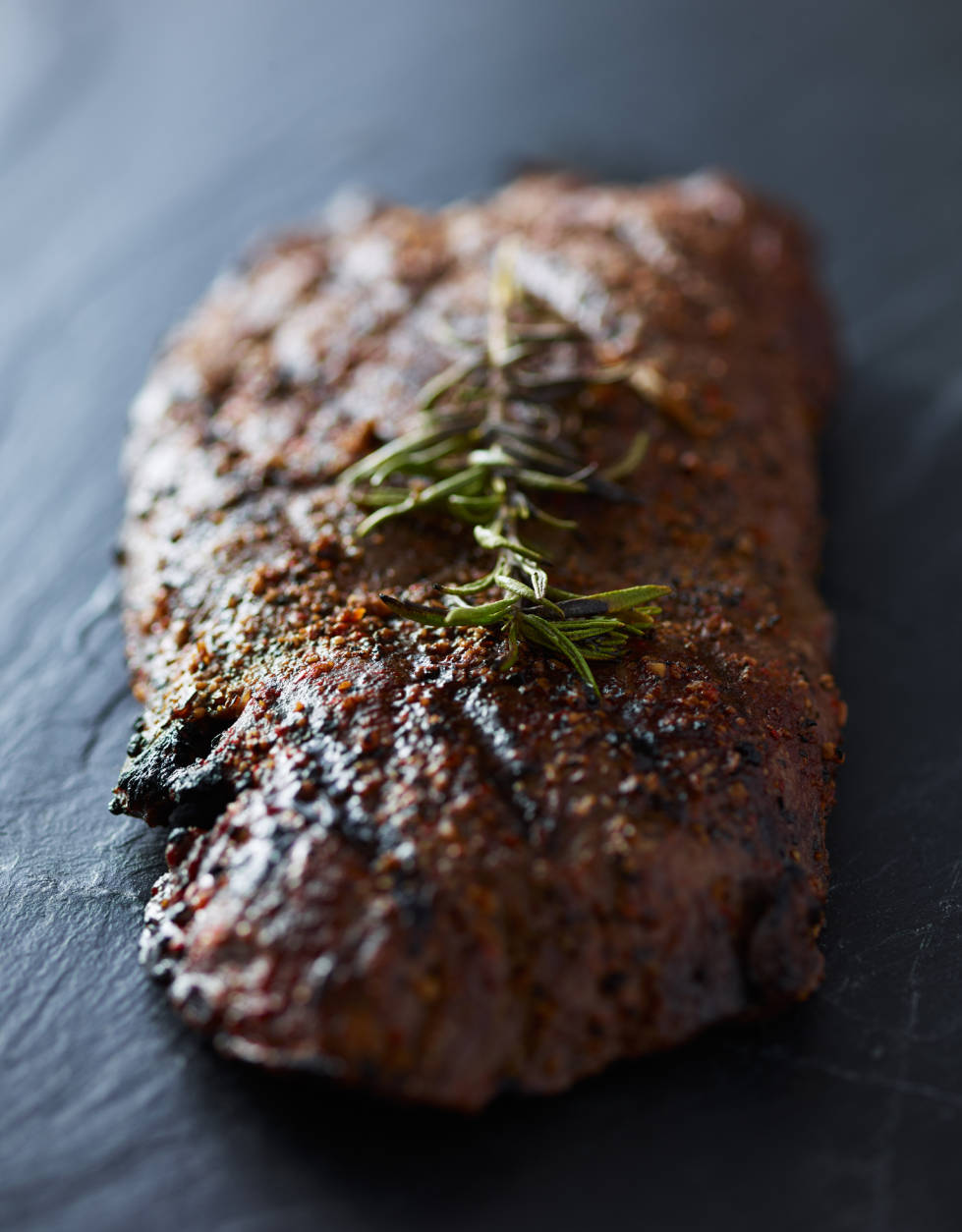 grilled flat iron steak resting on slate slab with rosemary garnish