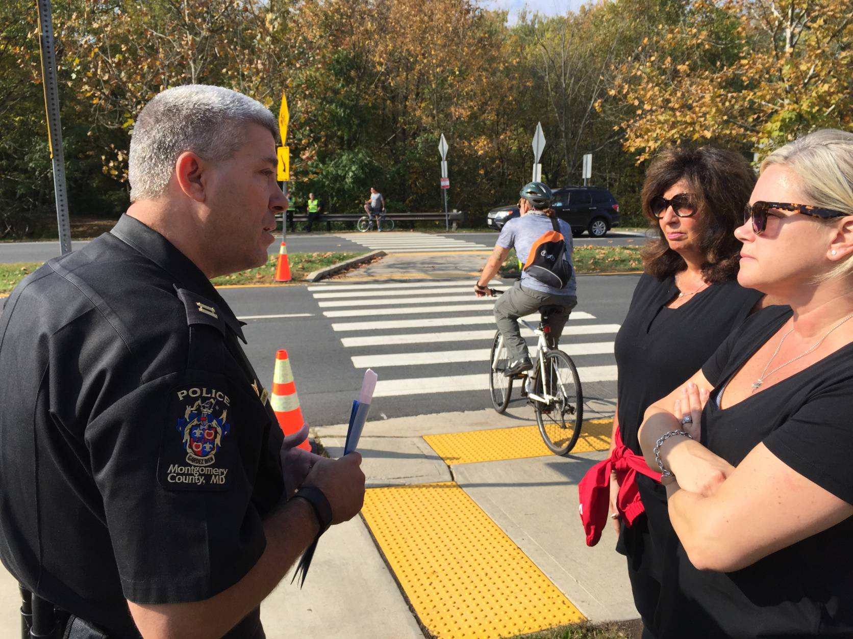 Tricia of Potomac and Margaret of Bethesda use the Capital Crescent Trail about three times a week. They're asking Montgomery County Police Captain Tom Didone why flashing lights aren't being added to the intersection to improve safety. (WTOP/Kristi King)