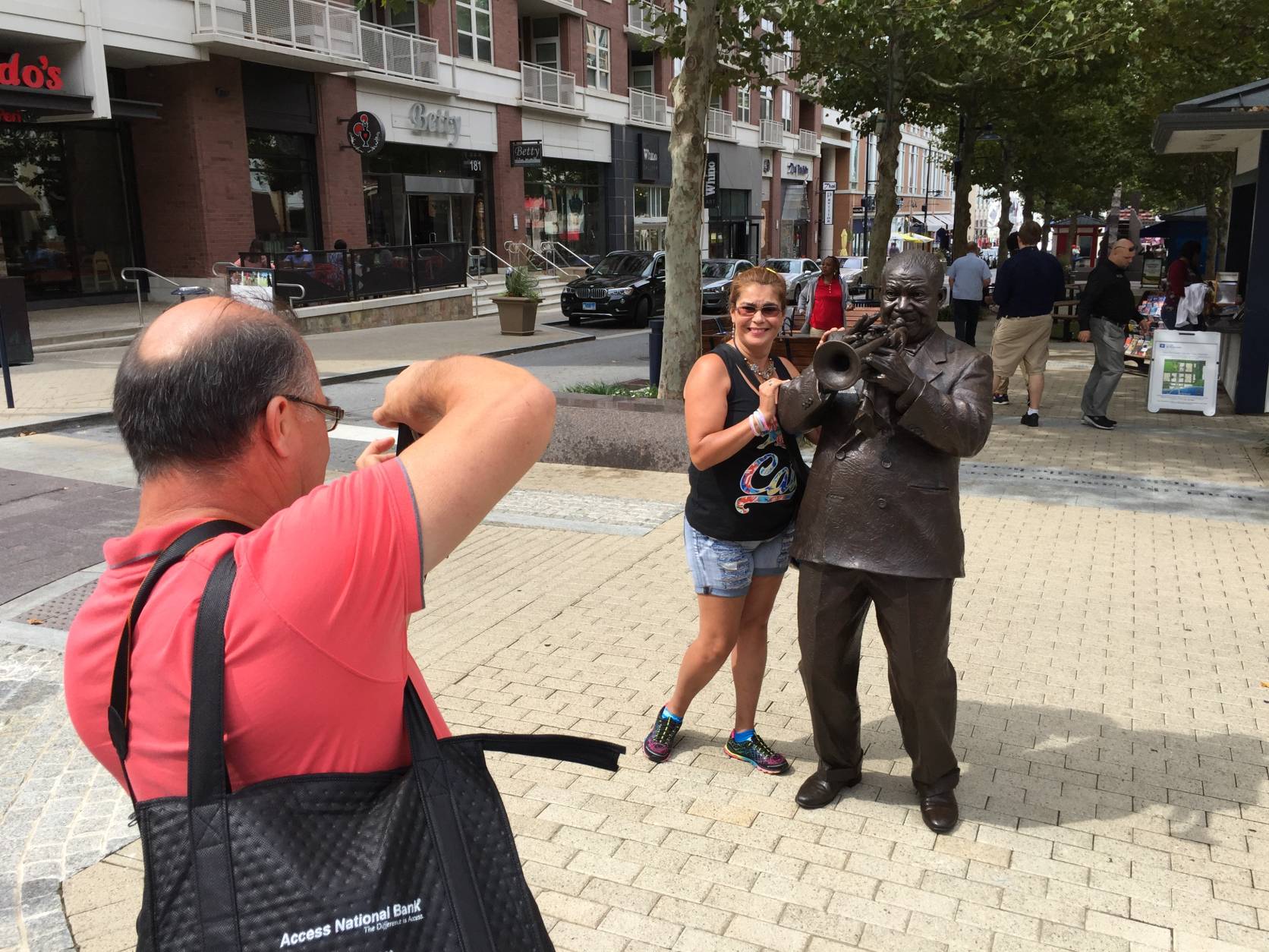 William Gullen, with the camera, was visiting National Harbor with a group of tourists from Peru. His friends didn’t know the trumpet playing statue depicts American jazz great Louis Armstrong. “We are surprised,” Gullen said of all the 
https://www.nationalharbor.com/art/
public art on display. (WTOP/Kristi King)
