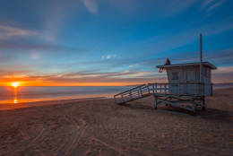Sunset on the beach in Southern California as a man sits on a Manhattan Beach lifeguard tower with Malibu in the background.