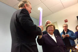Sen. Barbara Mikulski, the longest-serving woman in the history of Congress, passes the torch  -  a multicolored, flashing, battery-powered light bar - to her successor Chris Van Hollen on Wednesday morning in Baltimore  after her traditional post-electionb breakfast at an eatery near her Baltimore office. (WTOP/John Aaron)