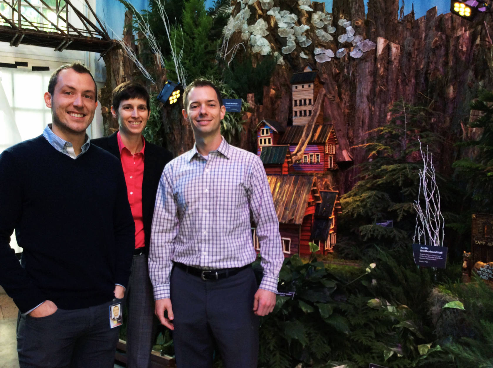 Devin Dotson (right) public affairs and exhibits specialist for the U.S. Botanic Garden, stands with two of his colleagues in front of a holiday exhibit feature. (WTOP/Hanna Choi)