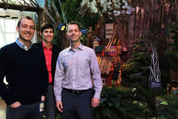 Devin Dotson (right) public affairs and exhibits specialist for the U.S. Botanic Garden, stands with two of his colleagues in front of a holiday exhibit feature. (WTOP/Hanna Choi)