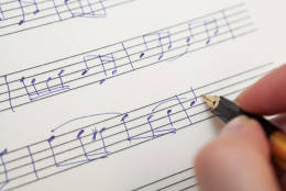 Hand pointing with pen to music book with handwritten notes