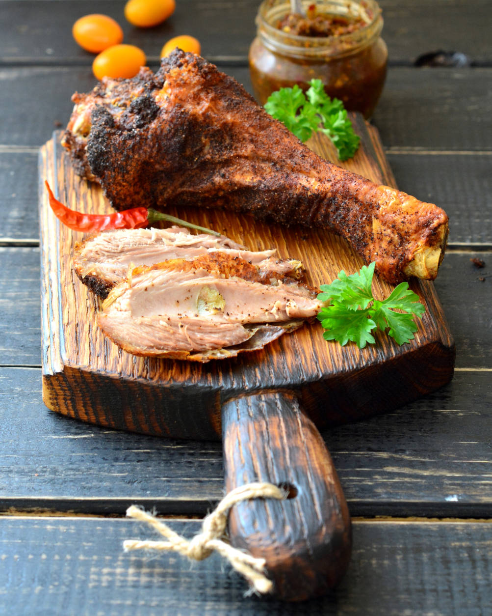 Roast turkey drumstick on a dark wooden table with tomatoes, herbs and spicy sauce