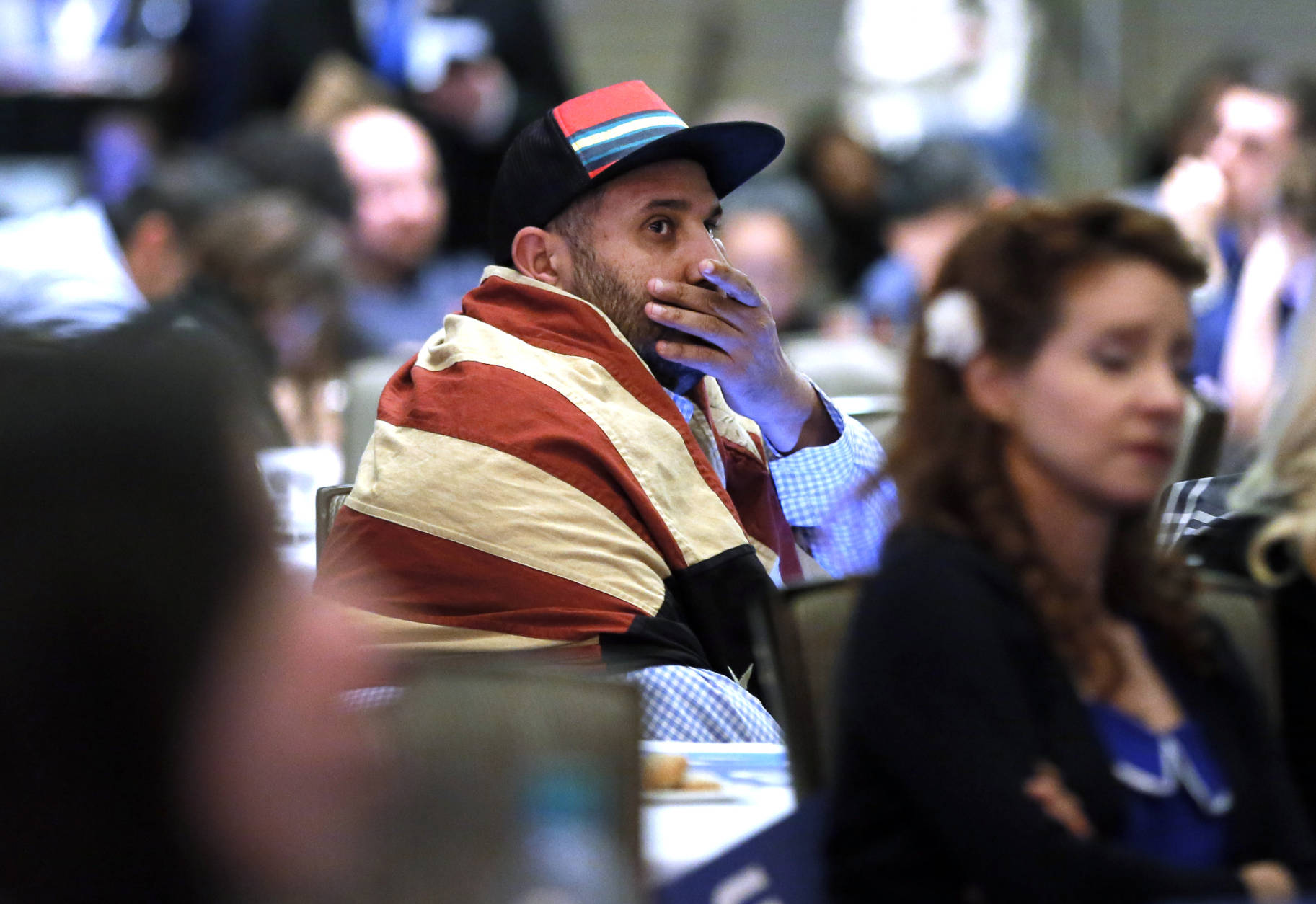 Khaled Nasr of Boston, sits wrapped in an American flag as he watches returns on a nearby large projection screen during the Dallas County Democrats watch party, Tuesday Nov. 8, 2016, in Dallas. (AP Photo/Tony Gutierrez)