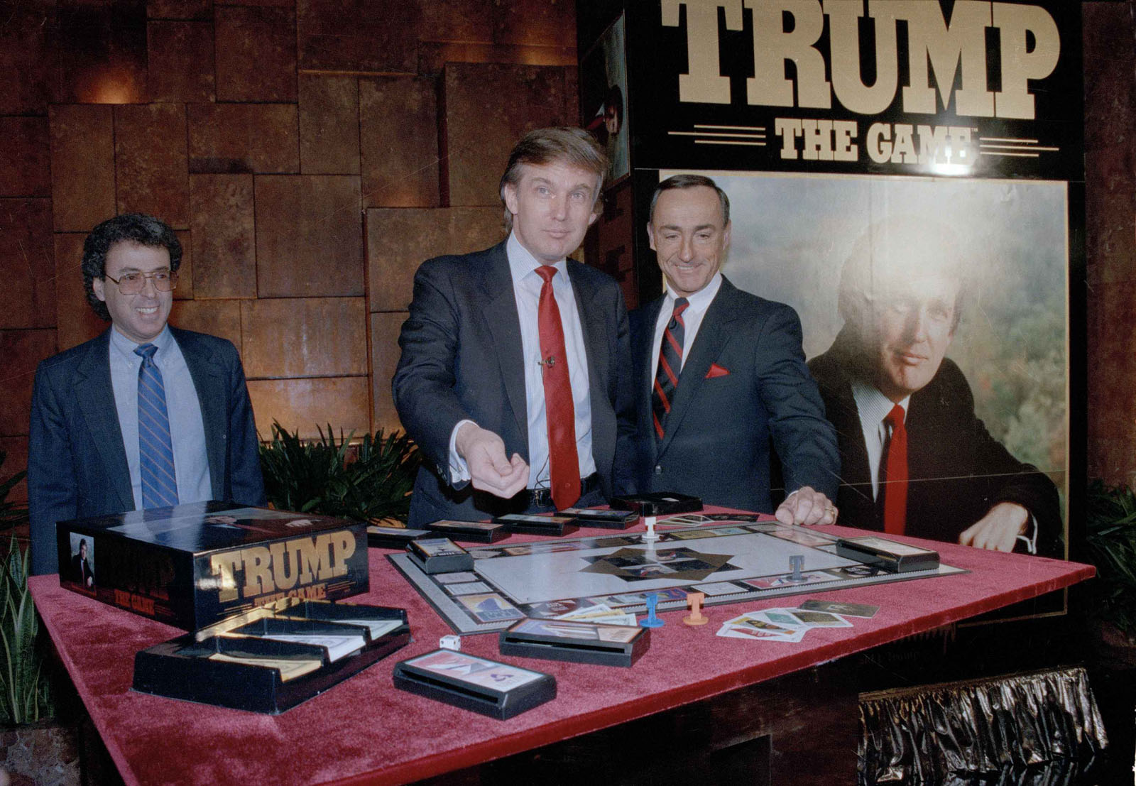 Real estate mogul Donald Trump, left, takes his turn as George Ditomassi, president of the Milton Bradley company, looks on at a news conference in New York, announcing a new board game, "Trump, The Game," Feb. 7, 1989. The game allows players to bid against each other and make deals for big ticket real estate. Man at far left is unidentified. (AP Photo/Mario Suriani)