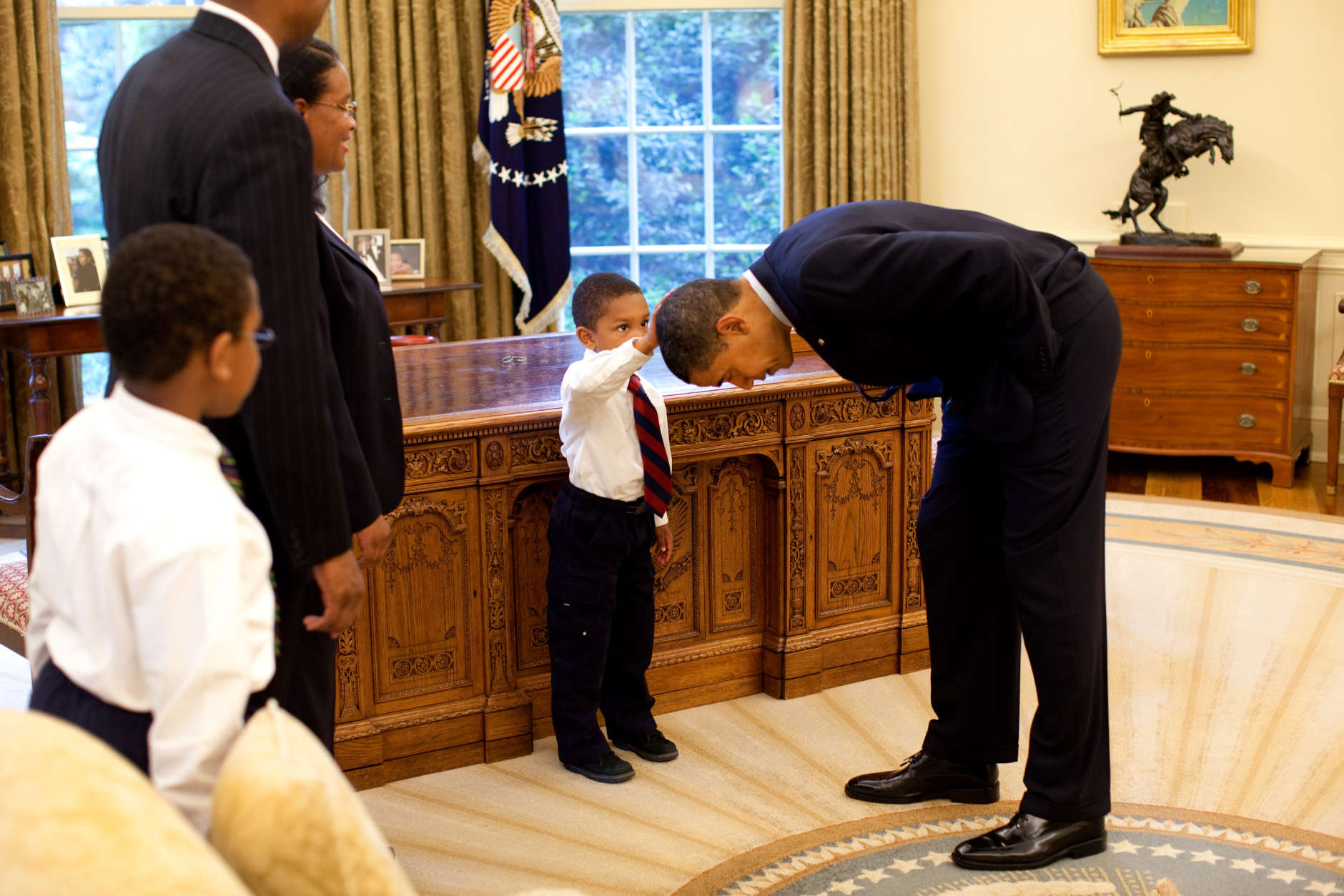 President Barack Obama bends over so the son of a White House staff member can pat his head during a visit to the Oval Office May 8, 2009.  Official White House Photo by Pete Souza.  This official White House photograph is being made available for publication by news organizations and/or for personal use printing by the subject(s) of the photograph. The photograph may not be manipulated in any way or used in materials, advertisements, products, or promotions that in any way suggest approval or endorsement of the President, the First Family, or the White House.