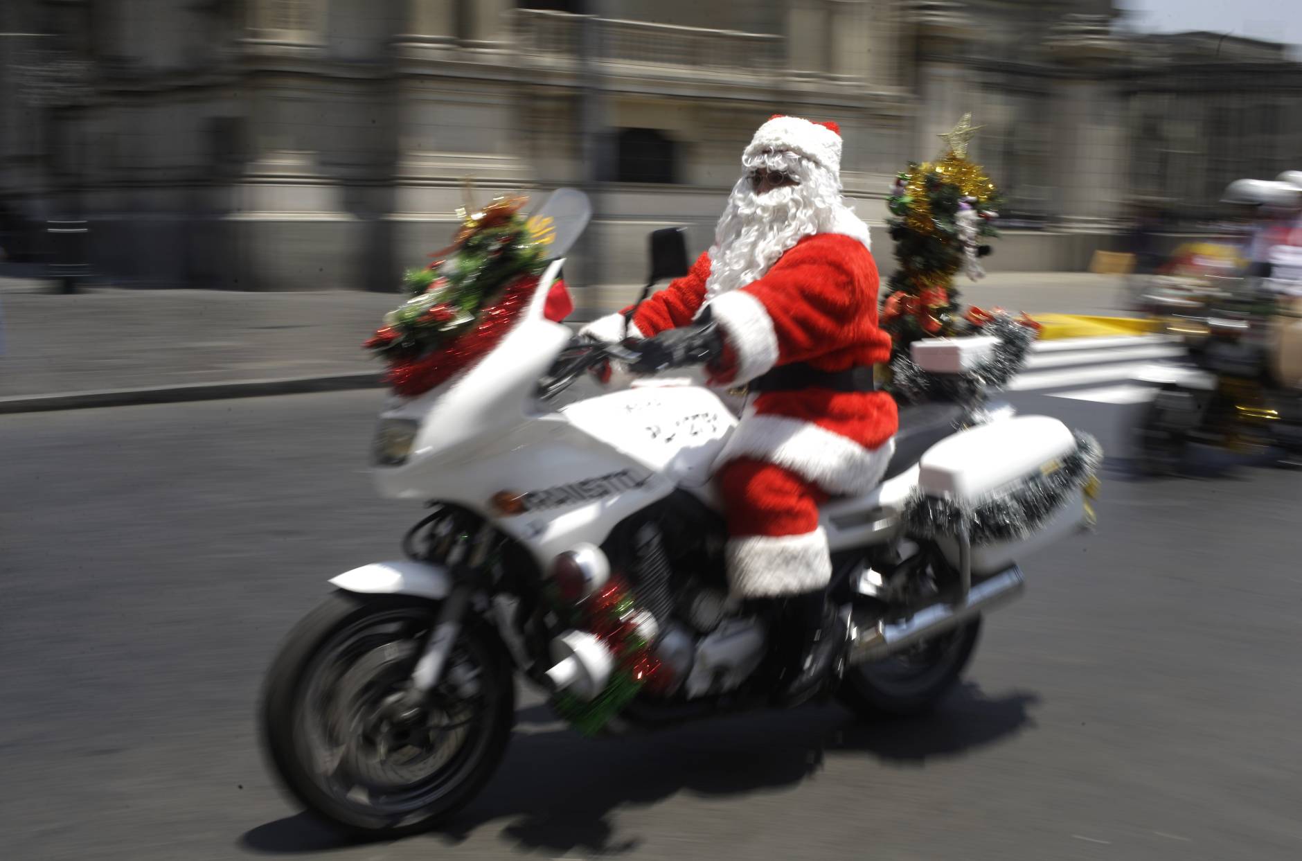 Traffic police officer Marco Chira, dressed in a Santa Claus costime, rides his motorcycle outside the government palace in downtown Lima, Peru, Tuesday, Dec. 20, 2016. The capital's traffic cops dressing as Santa and his helpers is an annual holiday ritual for the police department. (AP Photo/Martin Mejia)