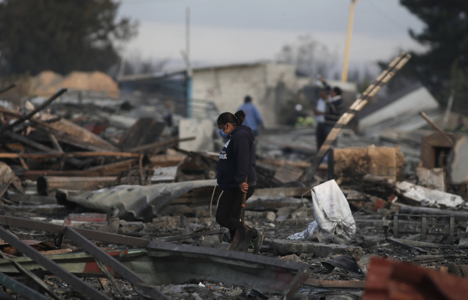 A woman carries a shovel as she walks through the scorched ground of the open-air San Pablito fireworks market, in Tultepec, outskirts of Mexico City, Mexico, Tuesday, Dec. 20, 2016.  An explosion ripped through Mexico’s best-known fireworks market on the northern outskirts of the capital Tuesday, injuring scores and killing at least 9 people , according to Mexican Federal Police. (AP Photo/Eduardo Verdugo)