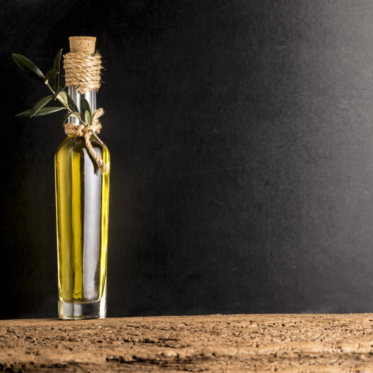 Extra virgin olive oil in rustic glass bottle on rustic background