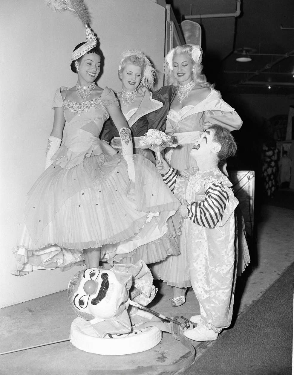With a princely gesture, circus midget Prince Paul presents flowers to three English girls who are in the show, backstage during the New York run, April 14, 1953. The girls are: left to right, Pat Cooper, who is from Devonshire; Shiley Coomas and Brinda Elliot, both of London. (AP Photo/VN)