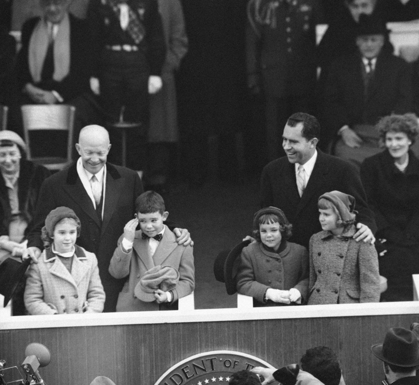 President Dwight D. Eisenhower regards with an amused smile the embarrassed salute given by his grandson, David, to a passing unit of the inaugural parade in Washington, Jan. 21, 1957. Vice President Richard  Nixon and his oldest daughter, Patricia, right, share the fun. David's sister, Barbara, is at left, and Vice President Nixon's youngest daughter, Julie, watches the paraders. (AP Photo)