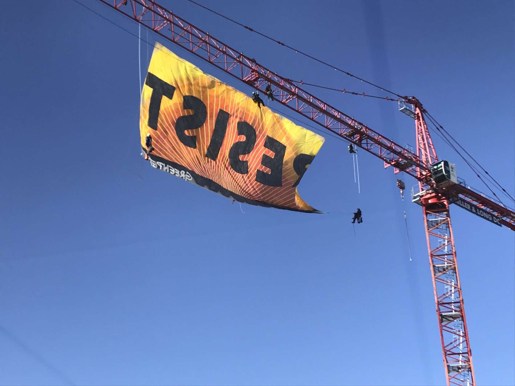 Protesters from Greenpeace unfurl a banner reading "Resist" on a construction crane in downtown D.C. Wednesday morning. (WTOP/Neal Augenstein)
