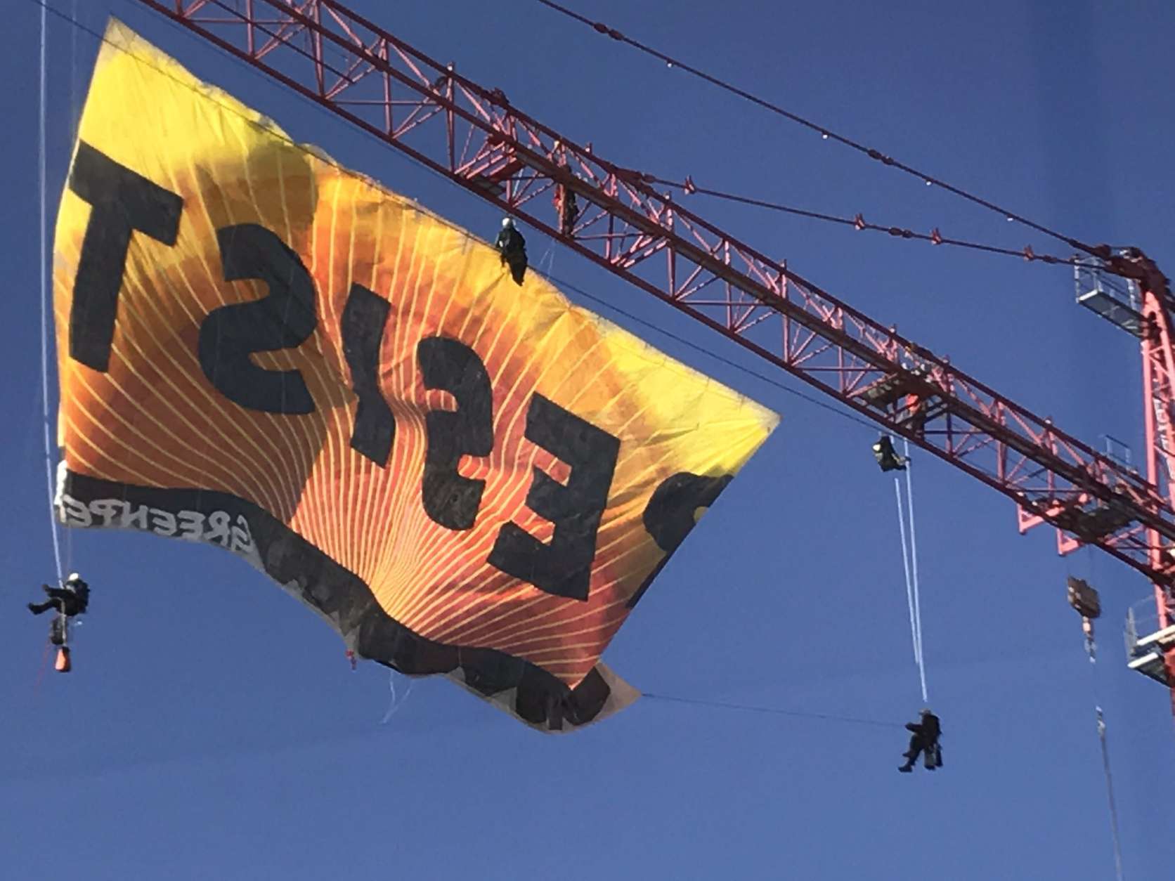 Protesters from Greenpeace unfurl a banner reading "Resist" from a construction crane in downtown D.C. Wednesday morning. (WTOP/Neal Augenstein)