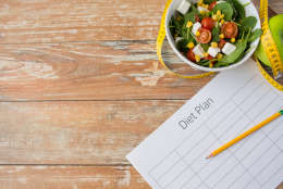 healthy eating, dieting, slimming and weigh loss concept - close up of diet plan paper green apple, measuring tape and salad