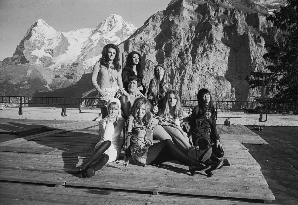 Australian actor George Lazenby poses with several of his female co-stars whilst filming the new James Bond film 'On Her Majesty's Secret Service' in the Swiss Alps, 22nd October 1968. From left to right, the actresses are (at the back) Helena Ronee, Zaheera, Catherina von Schell, (sitting) Anouska Hempel, Julie Ege, Joanna Lumley and Mona Chong. (Photo by Larry Ellis/Express/Hulton Archive/Getty Images)